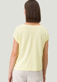 Kortærmet gul t-shirt lavet af blødt stof, med rund halsudskæring og en subtil søm, der løber lodret ned ad ryggen.