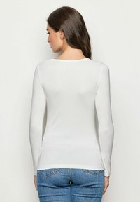 Weißes langärmliges Oberteil mit runder Ausschnitt, figurbetontem Schnitt und glatter Textur, kombiniert mit blauen Jeans.