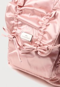 Vaaleanpunainen satiinireppu, jossa on kerrostettu pinta, nyörikiinnitys ja hopeinen logolevy. Ominaisuuksiin kuuluu sileä kangas ja tyylikäs muotoilu.