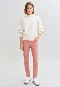 Crèmekleurige gebreide trui met hoge hals; roze ribfluwelen broek; witte sneakers. Eenvoudig ontwerp met geribbelde manchetten en zoom, gladde texturen.