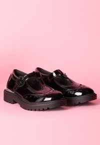 Pantofi din piele lacuită neagră cu vârf rotund, accent floral și design cu bretele în T. Talpă groasă din cauciuc cu textură.