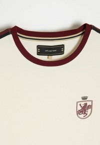 Kremowa koszulka z bordowym ściągaczem, z nadrukiem lwa z koroną. Metka z napisem "diverse", rozmiar L.