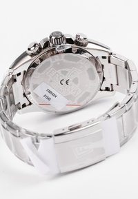 Montre chronographe en acier inoxydable argenté avec un fond de boîte transparent, disposant de trois poussoirs et d'une fermeture à clip.