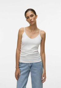 Canotta di cotone bianco con spalline sottili, caratterizzata da un design a V e una silhouette aderente. Abbinata a jeans in denim blu chiaro.