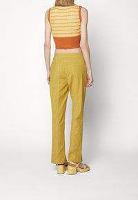 Stickad croptop med gult och orange mönster; högmidjade gula byxor med kontrasterande sömmar; gula klacksandaler med blockklack.