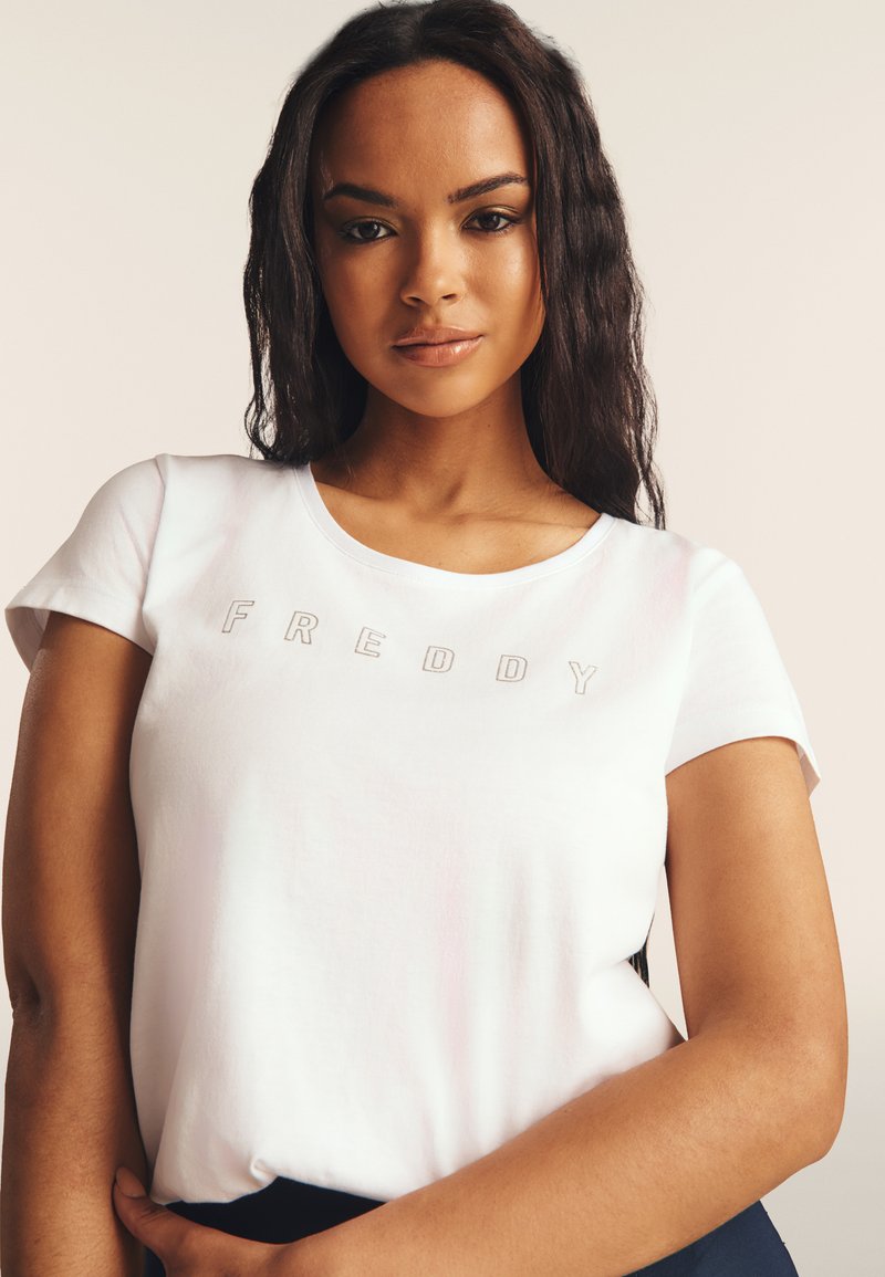 T-shirt bianca in cotone con maniche corte, scollo rotondo e scritta in rilievo "FREDDY" in grigio. Tessuto morbido con vestibilità comoda.