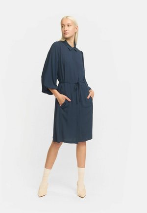 Rochie ușoară, de culoare albastru marin, cu guler, cordon la talie și buzunare laterale; are mâneci lungi, largi și un design până la genunchi.