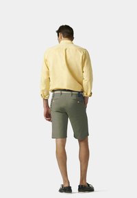 Chemise jaune à manches longues avec une finition texturée, associée à un short vert olive avec des poches latérales et des accents de ceinture contrastants.