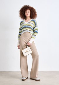 Multicolored striped sweater in green, blue, and white; beige high-waisted trousers; small white handbag with gold chain; silver shoes.