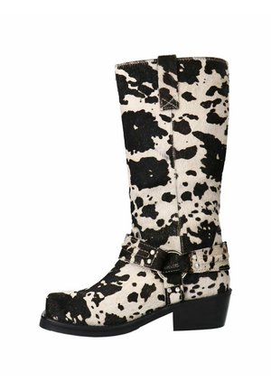 Black and white cow-print knee-high boots made of soft material, featuring a buckled strap detail and a block heel for stability.
