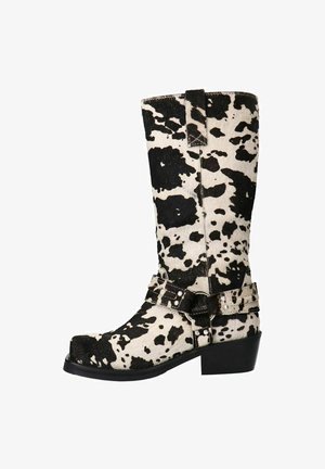 Black and white cow-print knee-high boots made of soft material, featuring a buckled strap detail and a block heel for stability.