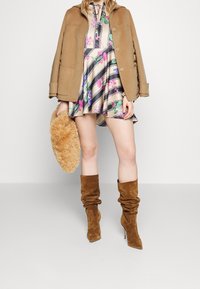 Lysebrun frakke over en blomsterprintet minikjole med striber; modellen holder en fluffy beigefarvet clutch og har brune ruskindsstøvler på.