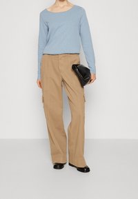 Světle modrý dlouhý rukáv, volné béžové cargo kalhoty s bočními kapsami a černá dámská kabelka. Černé boty dokončují outfit.