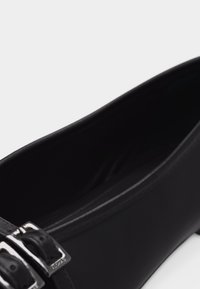 Μαύρο δερμάτινο παπούτσι με χαμηλή σόλα, δύο ασημένιες αγκράφες μπροστά και στρογγυλή μύτη.