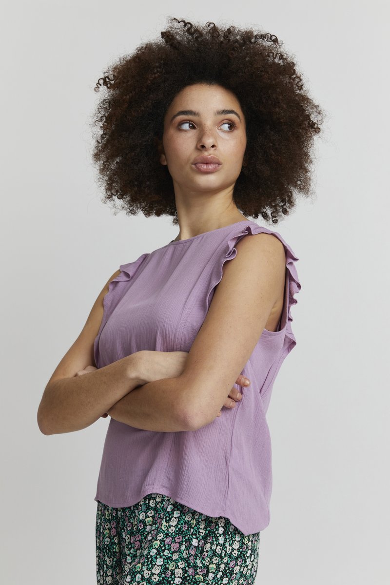 Top senza maniche lilla con dettagli arricciati sulle spalle e una finitura texture, abbinato a pantaloni floreali con uno sfondo scuro.