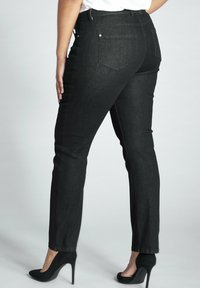 Pantalones vaqueros de mezclilla negra con corte ajustado, que cuentan con bolsillos traseros, detalles de costura mínimos y una textura suave, acompañados de tacones altos negros.