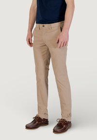 Chinos beige de algodón, con un corte ajustado, bolsillos laterales y cierre de botón. Combinados con zapatos tipo barco marrones.