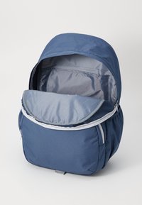 Sac à dos bleu marine avec un haut arrondi, fermeture éclair, et doublure intérieure grise. Présente une poche avant et un extérieur en tissu doux.