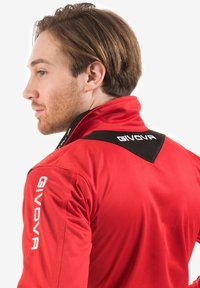 Giacca sportiva rossa con un design triangolare nero sul colletto posteriore. Include il logo bianco "GIVOVA" sulla spalla e sulla manica.