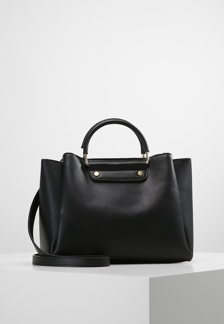 Sac à main en cuir noir avec des poignées courtes arrondies et une longue bandoulière réglable, posé sur une surface blanche.