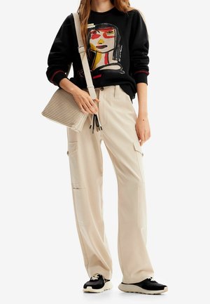 Sudadera negra con gráfico colorido, pantalones cargo beige con bolsillos laterales, bolsa gris claro con superficie texturizada, zapatillas negras y blancas.