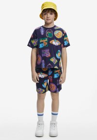 Short-sleeved purple shirt and shorts set with colorful graphic patterns; paired with a yellow bucket hat and white sneakers with blue stripes.
