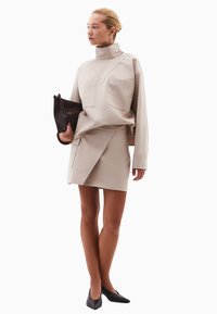 Beige sweatshirt med høj krave og to brystlommer, parret med en matchende asymmetrisk mini nederdel. Sort clutch og spidse flade sko.