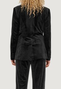 Blazer in velluto nero con una vestibilità su misura, dotato di uno spacco singolo sul retro e bottoni sui polsini, abbinato a pantaloni coordinati.