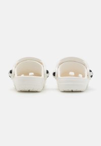 Tamancos de plástico moldado brancos com calcanhar fechado, com detalhes circulares pretos nas laterais e sola texturizada para maior aderência.