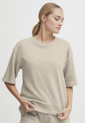 Beige oversized bomullssweatshirt med rund hals og korte ermer; har en ribbestrikket kant og mansjetter for ekstra tekstur.