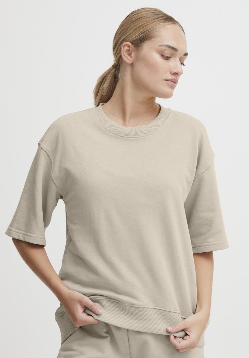 Beige oversized bomullströja med rund halsringning och korta ärmar; har ribbade avslut på fåll och ärm för extra textur.