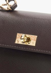 Tmavě hnědá kožená kabelka zblízka se zlatým kovovým zapínáním a texturovaným povrchem, s viditelným prošíváním a dekorativními detaily.