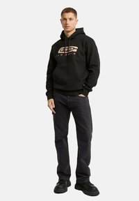 Felpa nera con cappuccio e tasca frontale, caratterizzata dalla stampa del logo multicolore "G-Star RAW". Abbinata a jeans grigio scuro e sneaker nere chunky.