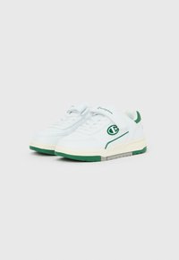 Άσπρα αθλητικά παπούτσια με πράσινες σόλες και λεπτομέρειες, λουρί velcro και το λογότυπο της Champion στο πλάι και στη γλώσσα, παρουσιάζονται σε απλό φόντο.