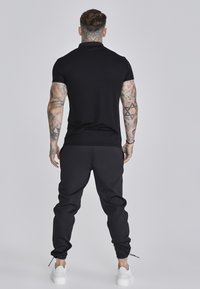 Camisa corta negra de manga corta, diseño ajustado, combinada con pantalones jogger negros, con piernas ajustadas y puños elásticos. Zapatillas blancas completan el look.