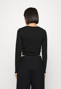 Černý top s dlouhými rukávy, kulatým výstřihem, přiléhavým střihem a ribbovanou texturou, kontrastující s černými širokými kalhotami s vysokým pasem.
