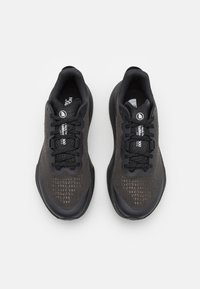 Baskets noires de sport avec une tige en mesh, bout rond et détails texturés. Présente des lacets noirs et une marque sur la languette et la semelle intérieure.