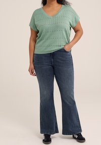 Top de manga corta y cuello en V de color verde menta con un patrón texturizado, combinado con jeans acampanados azul oscuro y zapatillas negras.