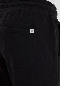Les joggeurs en coton noir présentent une poche cousue à l'arrière avec une petite étiquette blanche. La taille élastique offre une coupe décontractée.