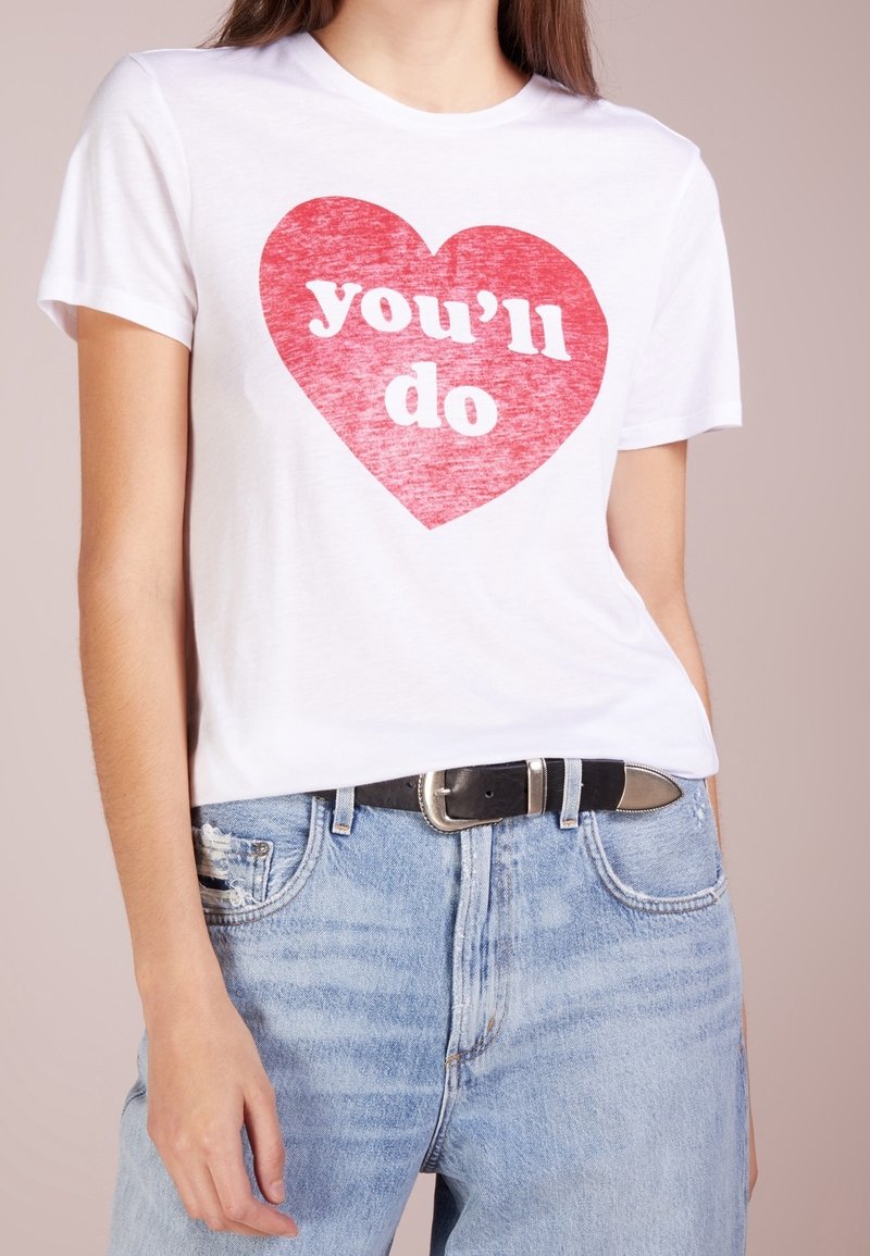 T-shirt en coton blanc avec un grand graphique en forme de cœur rouge et le texte « tu vas y arriver » en blanc. Associé à un jeans délavé bleu clair et une ceinture noire.