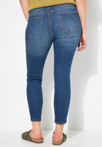 Modré džíny skinny s pěti kapsami, středním pasem a zkrácenou délkou. Nosené s plochými zelenými slip-on botami.