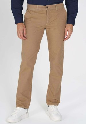 Pantalons en coton beige avec une coupe droite, dotés d'une fermeture à bouton à l'avant et de poches. Associés à des baskets blanches pour un look décontracté.