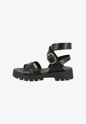 Black sandals feature a chunky sole, crossed straps at the front, and a wide ankle strap with a gold buckle detail.