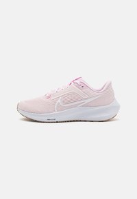Zapatilla de running Nike de color rosa claro con logotipo swoosh en blanco, parte superior de malla, entresuela blanca y suela de goma color marrón, mirando hacia la izquierda sobre fondo blanco.