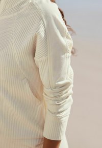 Suéter de canalé color beige claro que presenta una tela texturizada, mangas ajustadas y detalles de costura sutiles en los hombros y los puños.