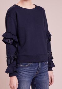 Sudadera azul marino con volantes de satén en las mangas, con un escote redondo y un estilo de corte relajado.