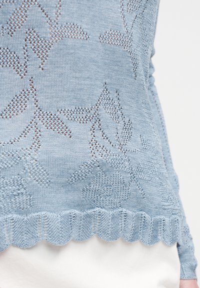 Haut tricoté bleu clair avec un motif floral, un ourlet dentelé et une texture ajourée. Le design est doux et détaillé.
