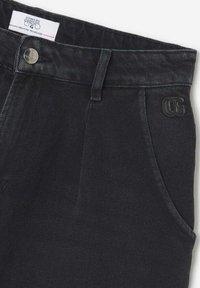 Pantalons en denim noir avec une texture lisse, présentant un design classique à cinq poches, une fermeture à bouton et un logo brodé sur la poche.