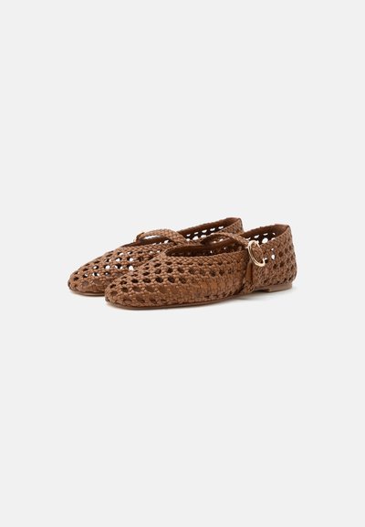 Chaussures plates tissées marron avec bouts fermés, brides croisées et détail de boucle dorée, présentées sur un fond clair uni.