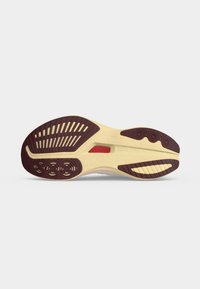 Η σόλα ενός δρομικού παπουτσιού Saucony που δείχνει υφασματοειδή σχέδια πέλματος σε καφέ, μπεζ και μια κόκκινη λεπτομέρεια σε ανοιχτό φόντο.